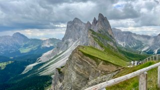 Expansive valley view from Seceda Dolomites with scattered clouds and green pastures.