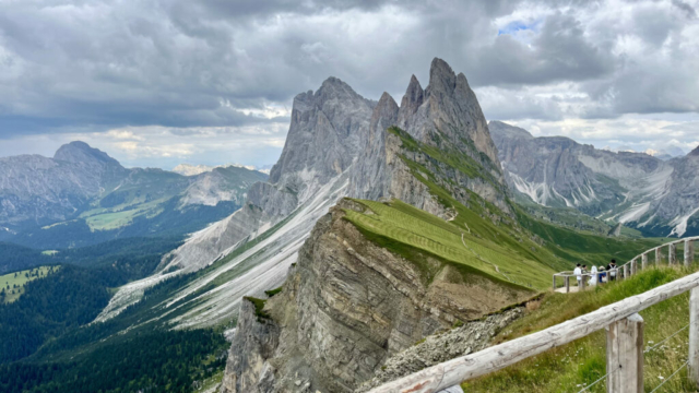 Expansive valley view from Seceda Dolomites with scattered clouds and green pastures.